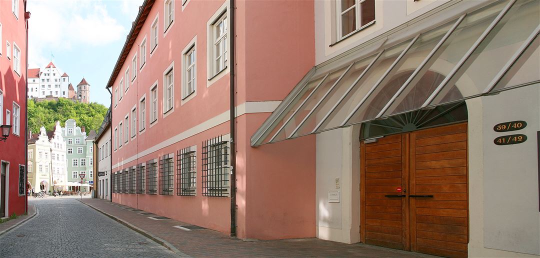 Blick auf das Geb&auml;ude der Volkshochschule Landshut mit Eingang von der L&auml;ndgasse aus. Am Ende der L&auml;ndgasse sind H&auml;user der Landshuter Altstadt zu sehen sowie die Burg Trausnitz auf dem Hofberg.