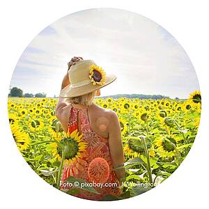 eine Frau mit Strohhut steht in einem Sonnenblumenfeld